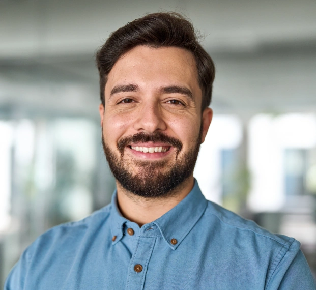 Smiling adult man with a beard wearing a blue shirt in a modern indoor setting.