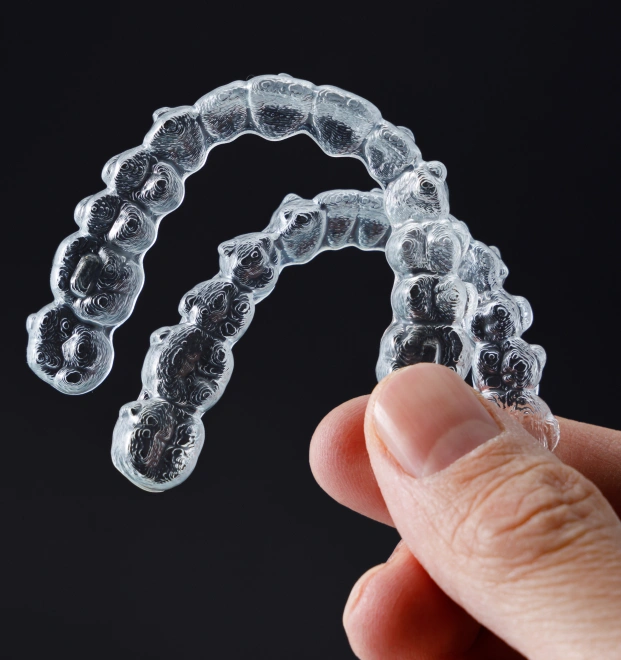 A hand holding clear aligners for cosmetic dentistry, showing the transparent orthodontic trays.
