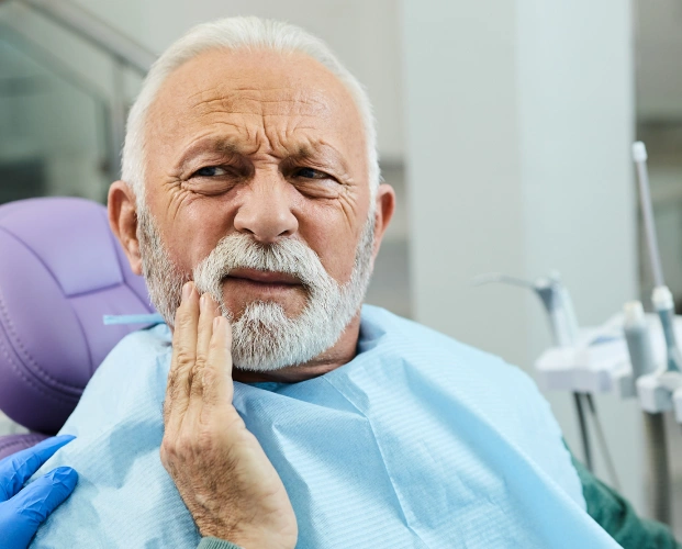 Senior patient experiencing jaw pain during TMJ evaluation at dental clinic.
